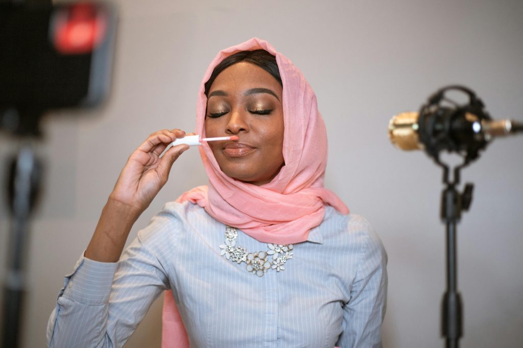 A beautiful Black Muslim woman in hijab reviews lipstick in an indoor setting for her vlog.