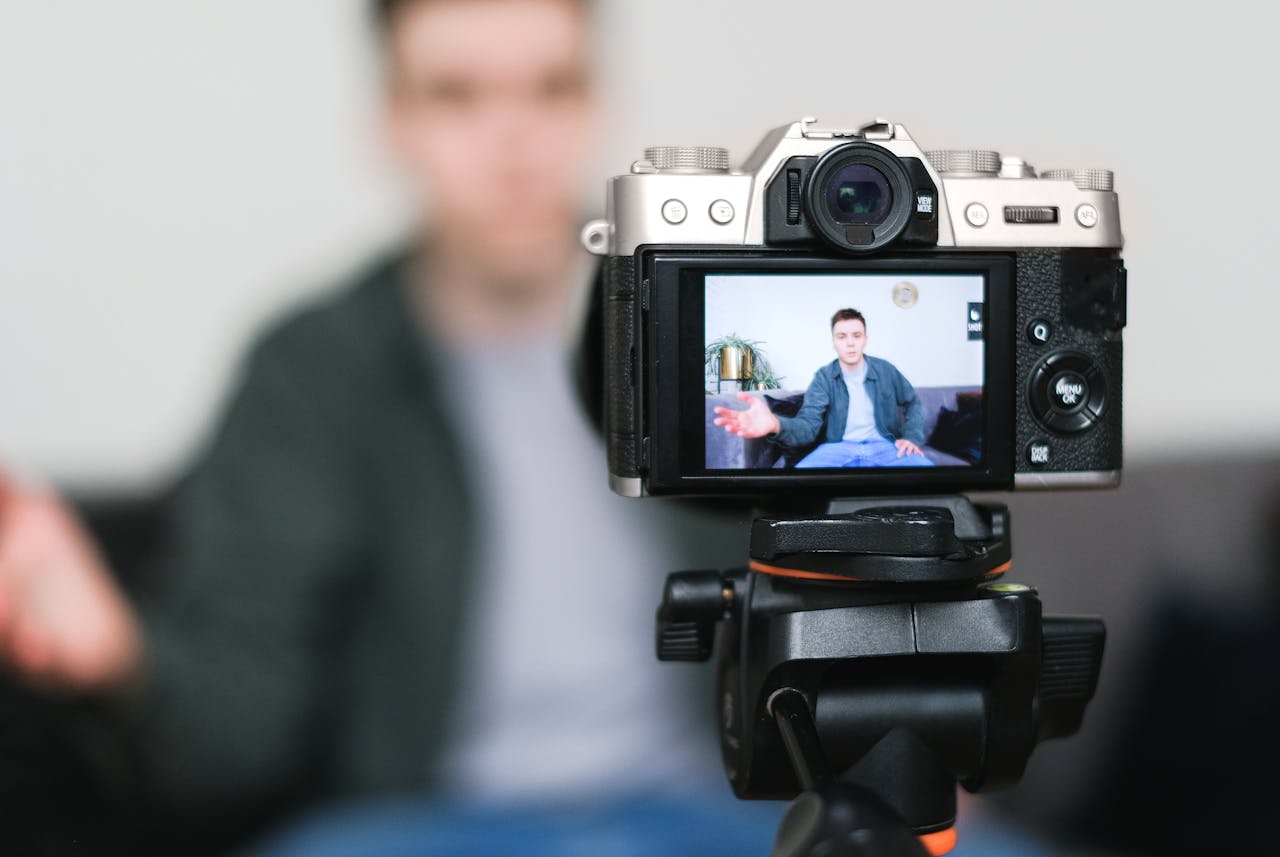 Man recording a vlog indoors using a mirrorless camera on a tripod with selective focus.