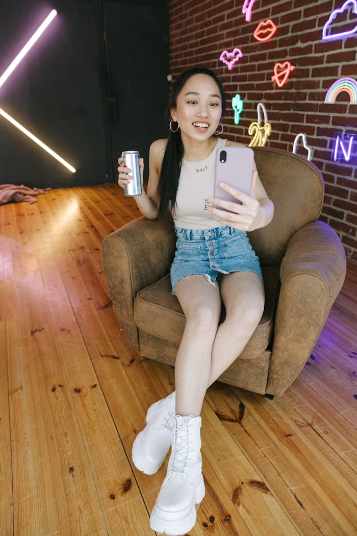 A young woman capturing a selfie while enjoying a drink, seated in a stylish indoor setup.