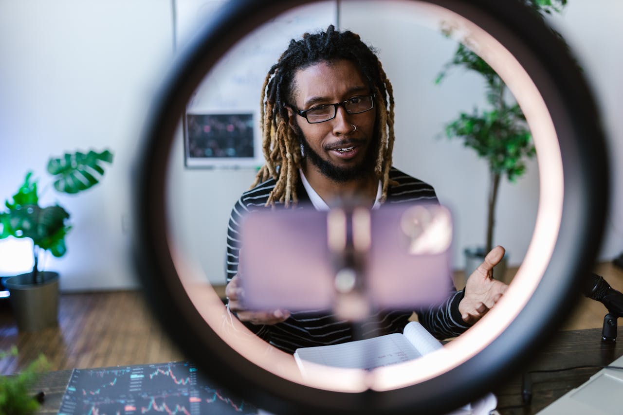 African American man using smartphone and ring light setup for vlogging indoors.